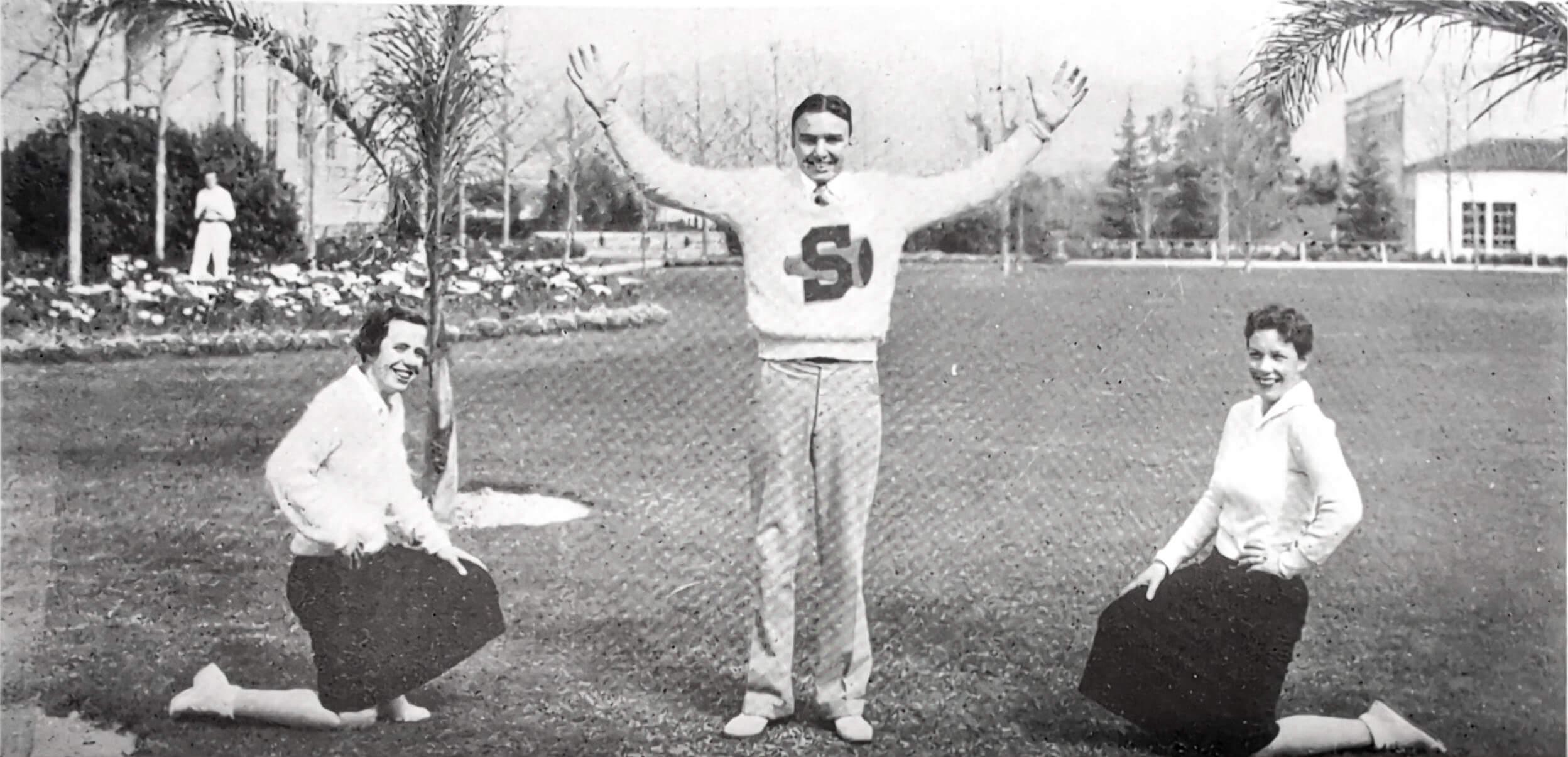 A student with an "S" sweater between two kneeling students. 