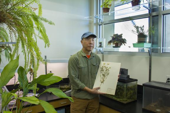 A photo of Mark Ikeda holidng a picture of a plant.